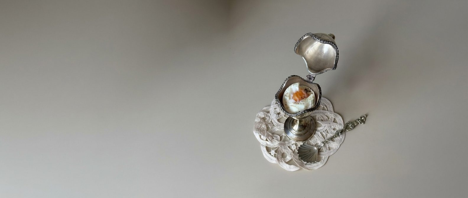 Silver plated vintage egg cup with a boiled egg, set on a lace doily with a small spoon